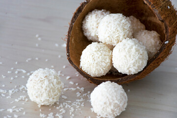 Fototapeta na wymiar Homemade sweets white coconut candy balls in nut shell on wooden background. Recipe of delicious white chocolate truffles in coconut flakes.