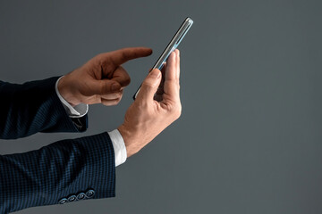 Hands of a businessman in a business suit holds a smartphone horizontally side view and presses the screen with his finger. Close-up.