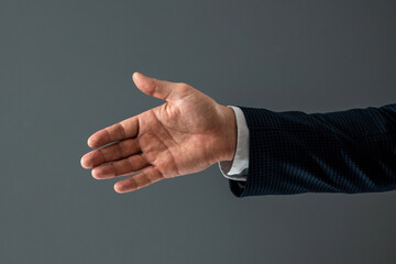 Male hand in suit shows thumbs up gesture on gray background. Concept ok, approval, close-up.