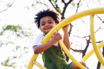 Cute African American little kid boy having fun while playing on the playground in the daytime in...