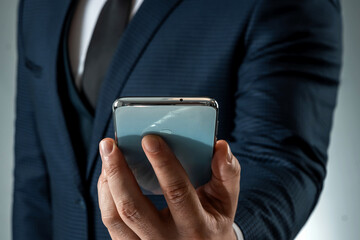 A businessman in a business suit holds a smartphone in his hands. Uses the Internet to work and communicate with partners. Online business concept, remote work, freelance. Close-up.
