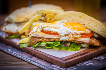 Milanesa argentinian steak sandwich with salad tomatoes cheese egg, chips and beer