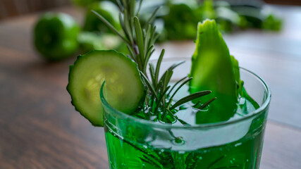 Green lemonade with cucumber and rosemary on wooden table.