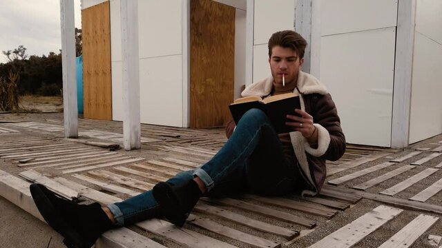 Ragazzo legge un libro e fuma una sigaretta seduto in riva al mare in spiaggia