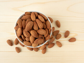 Organic almonds in ceramic bowl and heap almonds top view on wooden background for almond nuts can improve health concept.