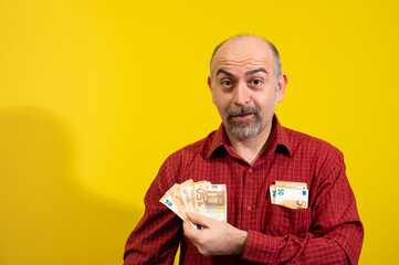 Middle-aged Caucasian man holding a bunch of 50 euro bills in his hand and has more in his shirt...
