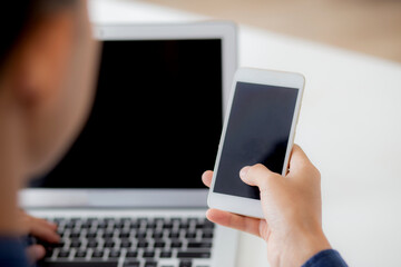 Hand of young man working with laptop computer and smartphone mockup on desk at home, notebook and phone display blank screen, freelance look message to internet, business and communication concept.