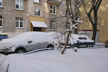 Uncleaned courtyards with heavy snowdrifts after snowfall in the city, cars under the snow.