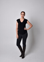Simple full length portrait of woman with red hair in a ponytail, wearing casual black tshirt and jeans. Standing pose facing front on, against a  studio background.