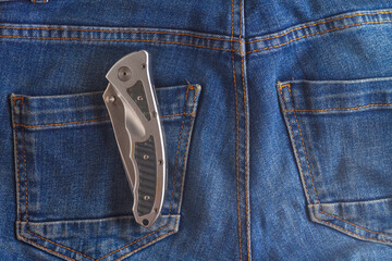 A folding knife made of durable steel is attached with a clip to the pocket of blue jeans