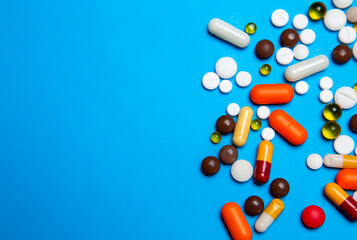 Scattered colored pills of pharmaceutical medicine, pills and capsules isolated on blue background. Coronavirus 2019-nCoV