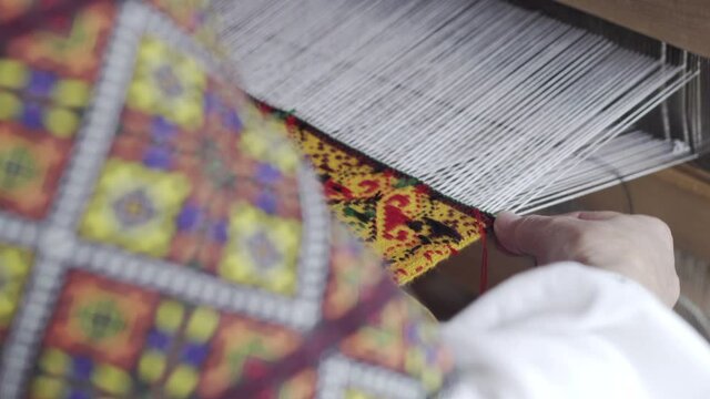 A woman in traditional embroidered clothes works behind a loom. Making a towel. Ukrainian folk art