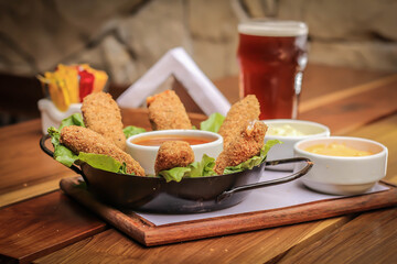 Cheese mozzarella sticks with spicy sauce dips and beer on a wood plank over a wooden table