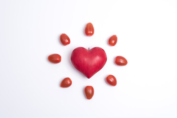 Top view on a red love heart, surrounded by small tomatoes and looking like a shining sun or a flower, white background. Concept of love and valentine's day