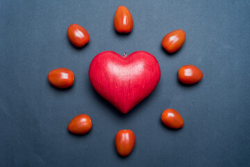 Red love heart, surrounded by small tomatoes and looking like a shining sun or a flower, black background. Concept of love and valentine's day