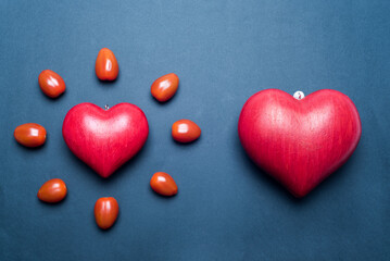 Red love heart, surrounded by small tomatoes and looking like a shining sun or a flower, black background. Concept of love and valentine's day