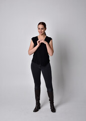 Simple full length portrait of woman with red hair in a ponytail, wearing casual black tshirt and jeans. Standing pose facing front on, against a  studio background.