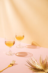 Celebration creative concept with two glass of wine drink, gold fork and  palm leaf. Nice shadow on the pastel pink and yellow background.