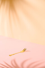 Minimal creative concept of single gold fork against nice pastel pink background with palm leaves shadow in the corners. Celebration idea