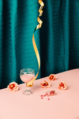 Minimal after party concept with pink drink in the wine glass with gold celebration ribbon and rose flowers around. Pills or sweet candy lay all over with small bottle full of them