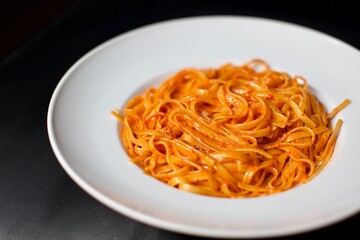 cream spaghetti with tomato sauce in a white porcelain plate. Close up view and black, blurry background.