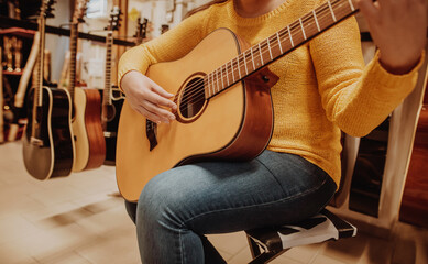 Jonge vrouw die een nieuwe houten gitaar probeert en koopt in een muzikale instrumentale winkel of winkel