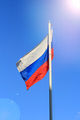 Photo developing the wind Russian flag on the blue sky. National flag on the background of sunbeams