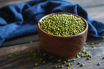 Healthy superfood. Uncooked green mung beans in wooden bowl on wooden background. Close-up.