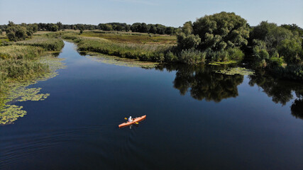 Aerial view of young man floats on an orange kayak on the river. The banks of the river are overgrown with reeds. Ukraine