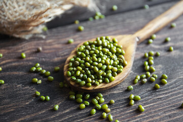 Healthy superfood. Uncooked green mung beans in wooden spoon on wooden background. Close-up..