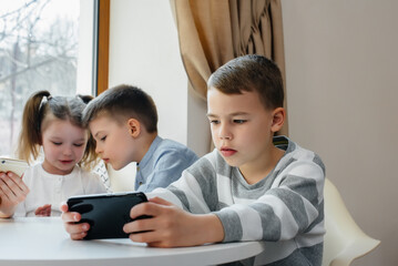 Children sit at a table in a cafe and play mobile phones together. Modern entertainment