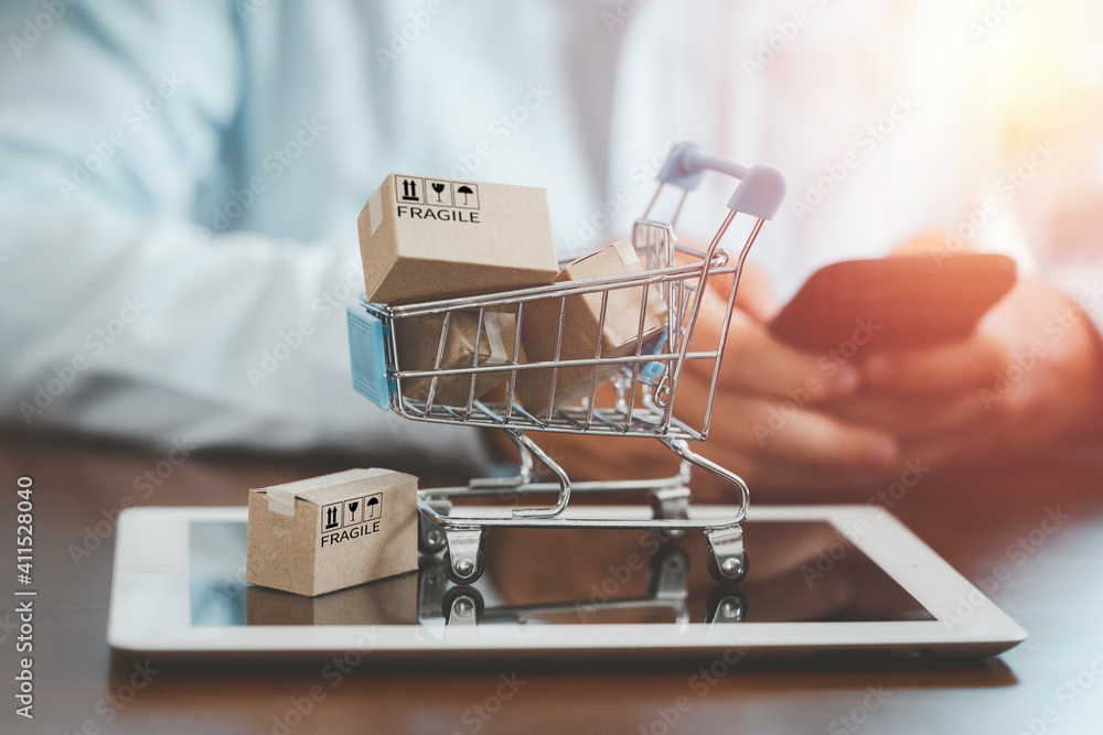 Poster small cartons box with shopping trolley on tablet and shopper use smartphone to input order for onli