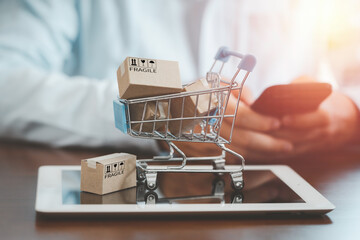 Small Cartons box with shopping trolley on tablet and shopper use smartphone to input order for...