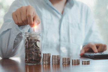 Businessman using calculator and putting coin to saving jar and coins stacking , deposit money...