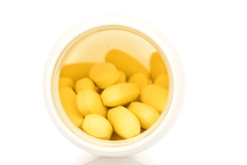 Several oval yellow pills with a white plastic box, close-up, isolated on white.