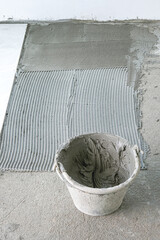 gray cement cream in can on floor house site. prepare equipment for install tiles white color....