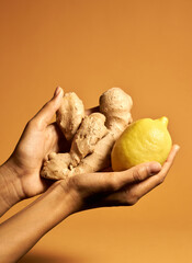Studio shot of female hand holding yellow lemon and ginger root isolated over orange background....
