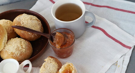 Round buns with filling in a natural wicker plate for tea and apple jam on a gray background. Ready to eat. Home cooking concept.