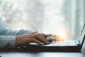Lightbulb glowing and businessman using computer laptop to input business strategy, creative thinking ideas and innovation concept.