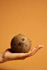 Studio shot of coconut fruit on female hand isolated over orange background. Healthy lifestyle concept