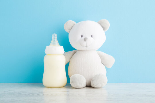 Teddy bear and bottle of white milk on wooden table at light blue wall background. Pastel color. Baby feeding concept. Closeup. Front view.