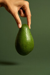 Studio shot of female hand holding ripe avocado isolated over green background. Vegan food, healthy lifestyle concept