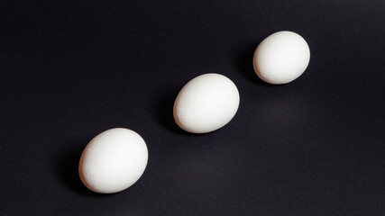 Three white eggs on a black background, dietary and healthy food rich in protein.