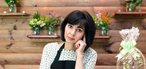 Portrait of a female florist at the workplace among flowers on a wooden background.