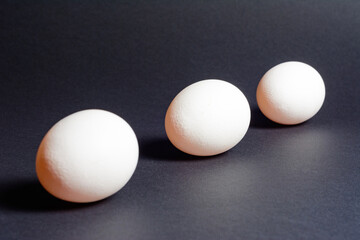 Eggs on a black background, three eggs in a row, shadow on the background of eggs, healthy and diet food.