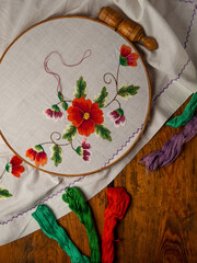 Flowers embroidery on white textile in hoop wooden background. Traditional ukrainian floss stitch...