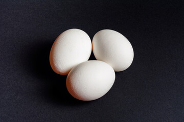 Eggs on a black background, three eggs in a row, shadow on the background of eggs, healthy and diet food.
