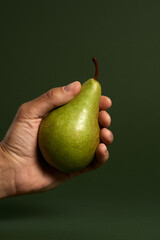 Studio shot of male hand holding ripe pear isolated over green background. Healthy eating and diet concept