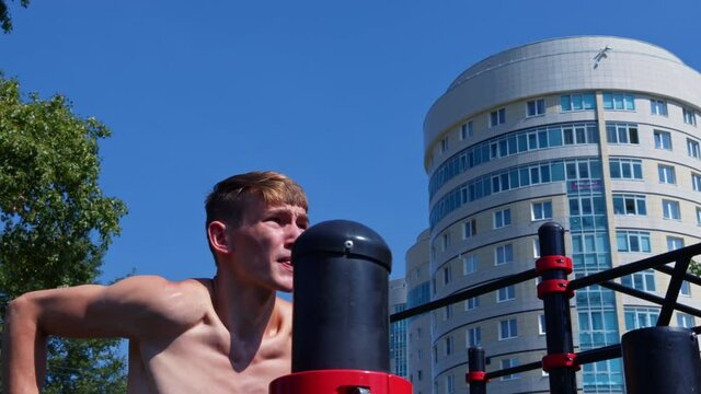 A man training outdoors on a summer day. A young sportsman is doing exercises on parallel bars at the sports ground