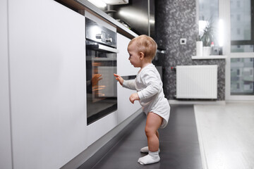 Infant baby boy near oven in home kitchen.